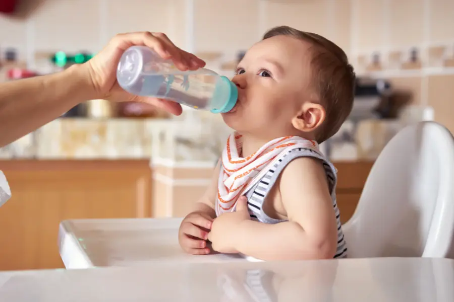 Warum ausreichendes Trinken im Alltag so wichtig ist 4 Baby trinkt aus Flasche im Hochstuhl als Beispiel für regelmäßige Flüssigkeitszufuhr im Alltag