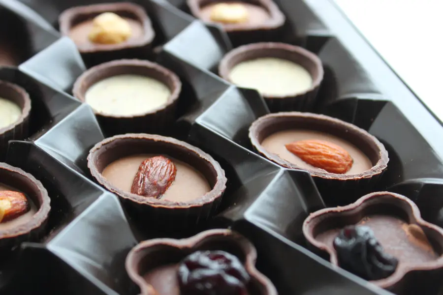 Handgefertigte Pralinen mit Mandeln und Fruchtfüllung Nahaufnahme von edlen Pralinen in einer schwarzen Pralinenschachtel, gefüllt mit Schokolade und verziert mit Mandeln und Früchten