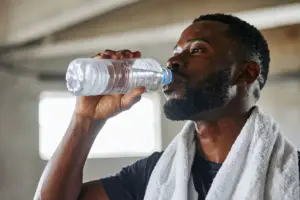 Sportler trinkt Wasser aus Flasche während Training als Beispiel für Flüssigkeitszufuhr bei körperlicher Belastung