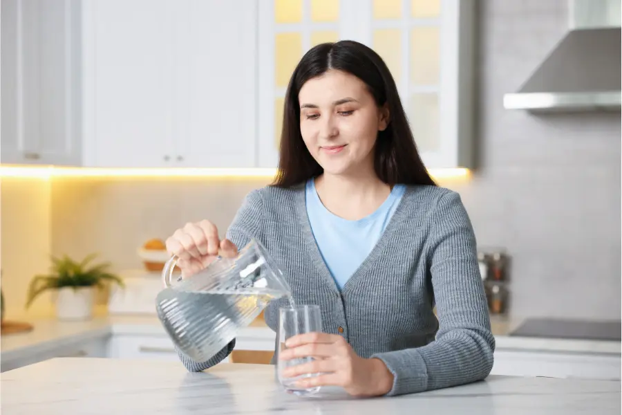 Warum ausreichendes Trinken im Alltag so wichtig ist 3 Frau schenkt Wasser aus Glaskaraffe in ein Glas in der Küche als Beispiel für regelmäßige Flüssigkeitsaufnahme