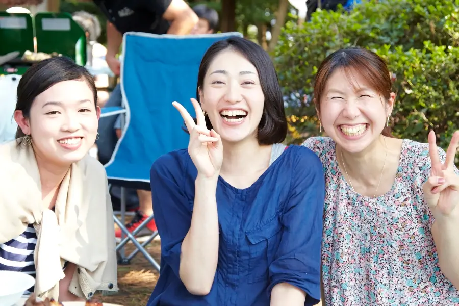 Drei lachende Japanerinnen im Freien. Der Valentinstag in Japan folgt einer besonderen Tradition: Frauen schenken Männern Schokolade – ein Brauch mit historischem Übersetzungsfehler als Ursprung. Drei fröhliche Japanerinnen lächeln in die Kamera und zeigen das Victory-Zeichen, aufgenommen im Freien bei einem Treffen.