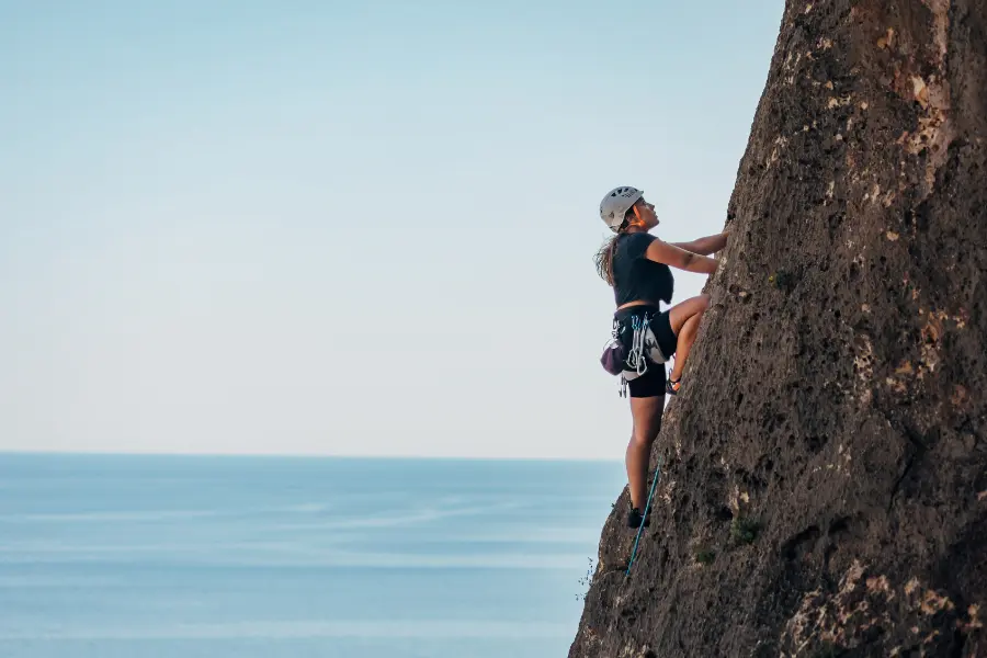 Sea-Trekking, CrossGolf & Co.: Diese Outdoor-Sportarten sind diesen Sommer ein Muss 1 Kletterin mit Helm und Klettergurt an einer steilen Felswand über dem Meer