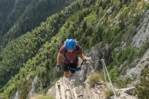 Kletterer mit Helm und Sicherung auf einem steilen Klettersteig in felsiger Berglandschaft