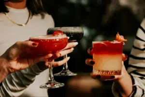Drei Personen stoßen mit farbenfrohen Cocktails und Mocktails in eleganten Gläsern an.