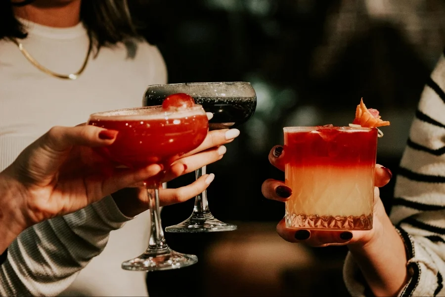 Drei Personen stoßen mit farbenfrohen Cocktails und Mocktails in eleganten Gläsern an.