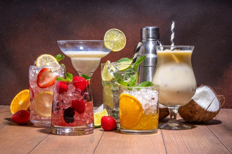 Mehrere fruchtige Cocktails mit Eis, Früchten, Minze und Kokosnuss auf einem Holztisch.