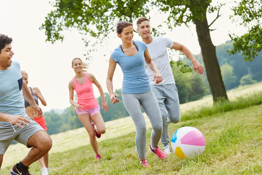 Gruppe junger Menschen spielt gemeinsam mit einem Ball auf einer Wiese im Park