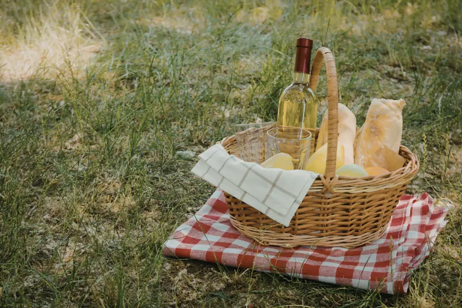 Picknickkorb mit Weinflasche, Gläsern und Baguette auf einer Decke im Grünen