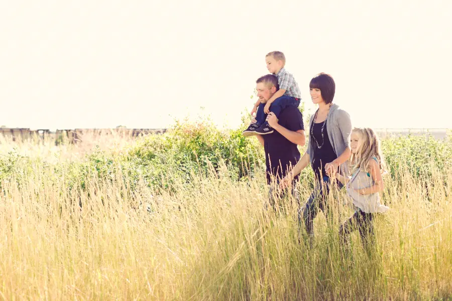 Fröhliche Familie mit heller, langer Kleidung spaziert durch hohes Gras in der Natur – ein Beispiel für effektiven Mückenschutz durch geeignete Kleidung im Alltag.