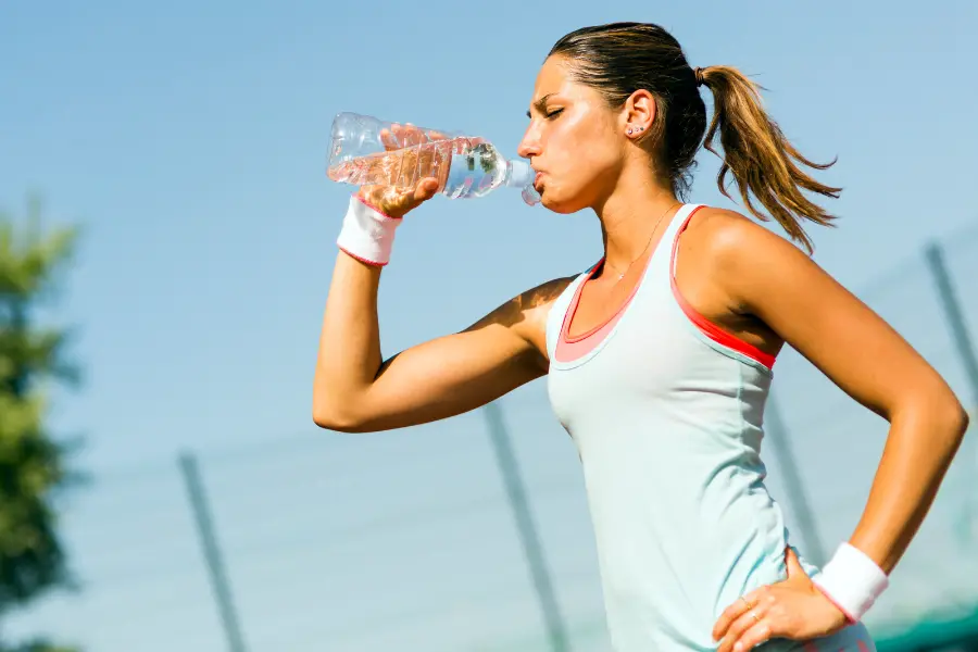 Jogging-Point Gutschein Sportlerin trinkt während einer Laufpause Wasser aus einer Trinkflasche und sorgt an einem sonnigen Tag für ausreichend Flüssigkeitszufuhr.