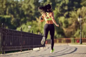 Sportliche Frau joggt auf einem gepflasterten Weg im Park. Sie trägt Sportbekleidung und läuft bei sonnigem Wetter – Symbolbild für Fitness, Ausdauertraining und einen aktiven Lebensstil.