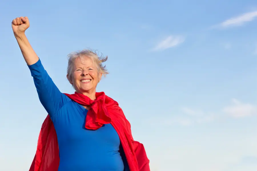 Tag der Senioren - was wir von unseren Großeltern lernen können 6 Lächelnde Seniorin mit blauem Oberteil und rotem Umhang hebt selbstbewusst die Faust in den Himmel – symbolisch für die Superkräfte, Lebenserfahrung und Stärke unserer Senioren.