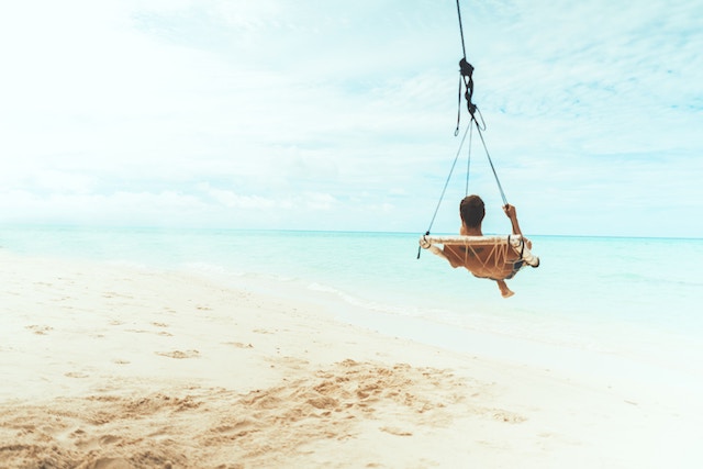 Ein Mann auf einer Schaukel am Sandstrand | Rabatte Coupon