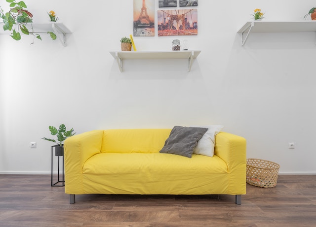 Eine gelbe Couch und an der Wand hängen nur zwei Regale | Rabatte Coupons