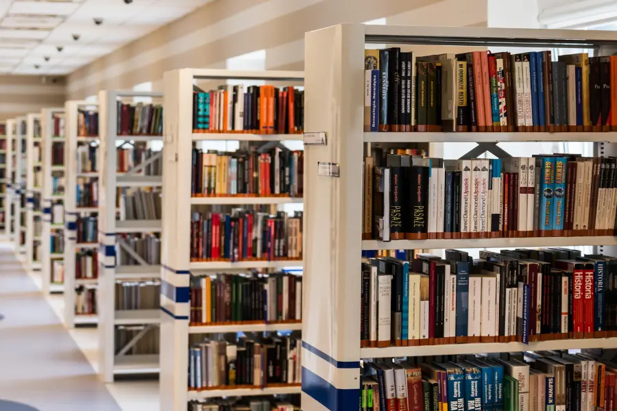 Helle Bibliothek mit mehreren Bücherregalen voller Bücher in langen Regalreihen.