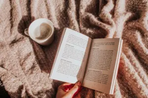 Geöffnetes Buch und Tasse Kaffee auf einer weichen Decke in gemütlicher Lesestimmung.