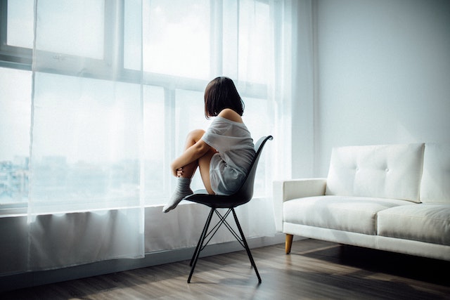 Eine Frau sitzt alleine auf dem Stuhl und sieht aus dem Fenster | rabatte coupons