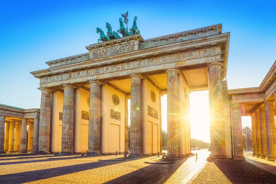 Brandenburger Tor in Berlin bei Sonnenuntergang mit goldenen Lichtstrahlen, historischen Säulen und der Quadriga auf dem Dach.