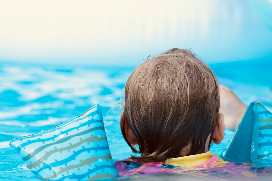 Kind schwimmt mit Schwimmflügeln im Pool
