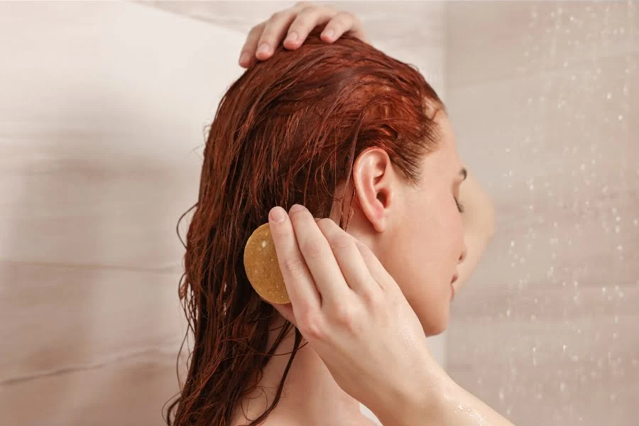 Person wäscht ihre Haare unter der Dusche mit einem runden festen Shampoo.