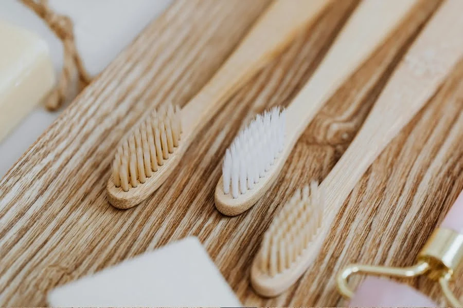 Zero Waste im Alltag - 5 einfache Tipps für's Badezimmer 3 Mehrere Bambuszahnbürsten liegen auf einer Holzoberfläche neben nachhaltigen Pflegeprodukten.