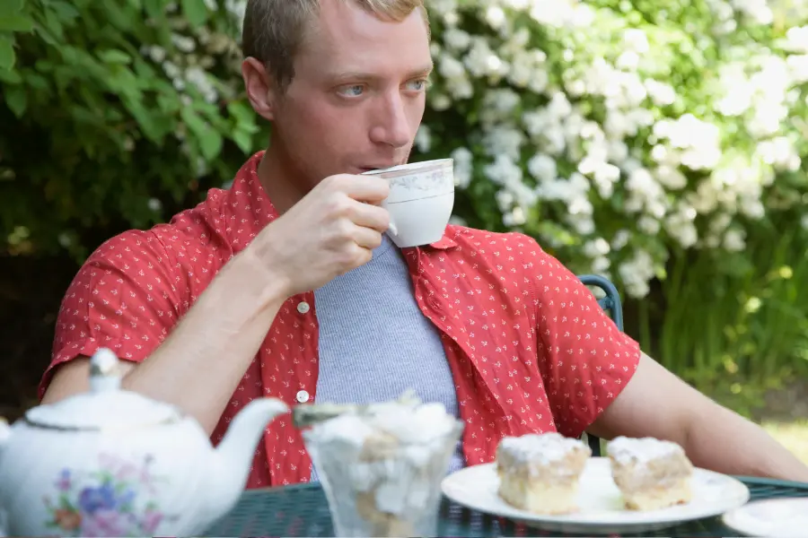 Diese Fakten über Teesorten und ihre Wirkung habt ihr sicher nicht gewusst | www.rabatt-coupon.com Mann trinkt im Sommer draußen im Garten eine Tasse Tee zu Gebäck und genießt eine entspannte Teepause.