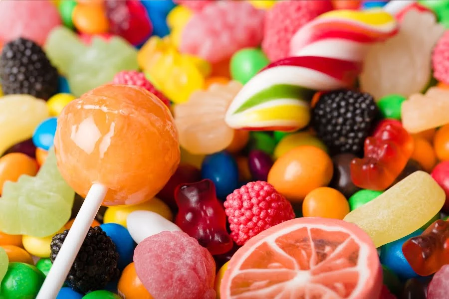 Gesundheitsrisiko Zucker 🐼 Ist die Zuckersteuer Debatte legitim? 3 Bunte Süßigkeiten mit Lutscher, Fruchtgummis und Bonbons als Symbol für hohen Zuckerkonsum
