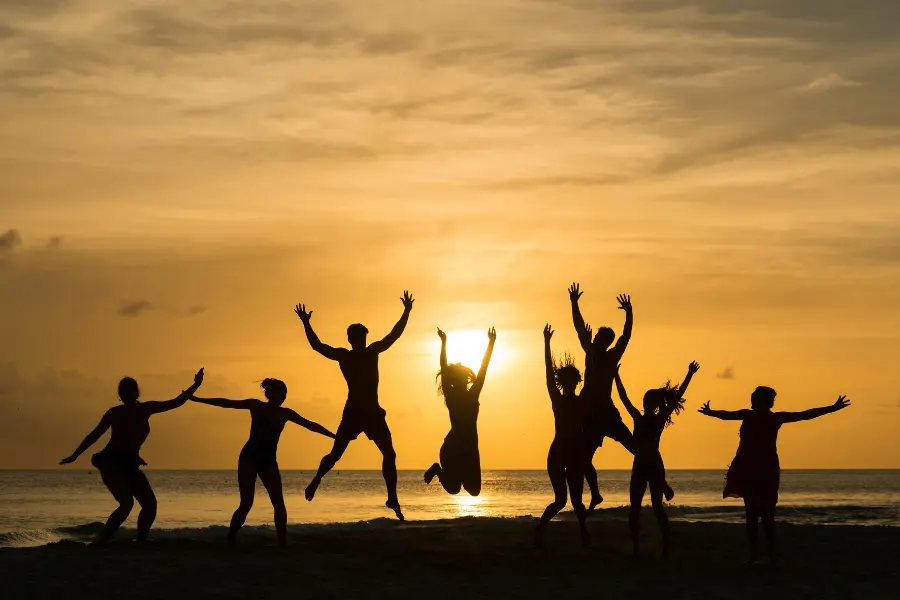 Mithilfe des Garten Und Freizeit Gutscheins lassen sich im Sommer die Aktivitäten mit Freunden günstig ausüben. Silhouetted group of friends jumping and celebrating on a beach at sunset.