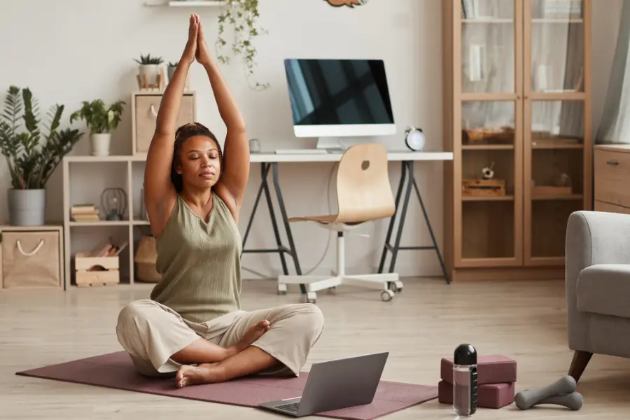 Jugendfussball und Corona ist nichts mehr für euch? Mit dem Check Jugendreisen Gutschein findet ihr tolle Alternativen zur Freizeitgestaltung für mit reduzierten Preisen. Woman practicing yoga on a mat at home with a laptop, water bottle, yoga blocks, and dumbbells nearby.
