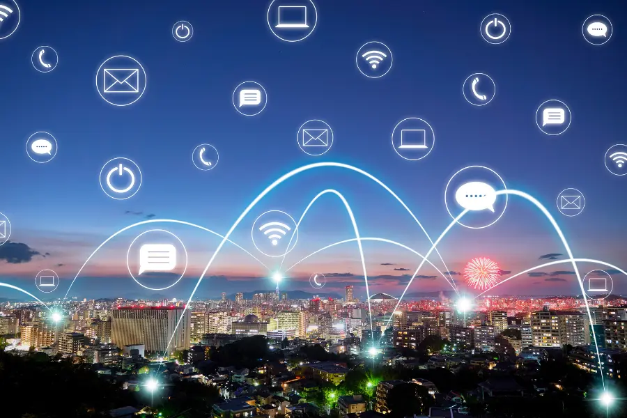 Smart city skyline at dusk with glowing digital communication icons and network connections above the urban landscape.