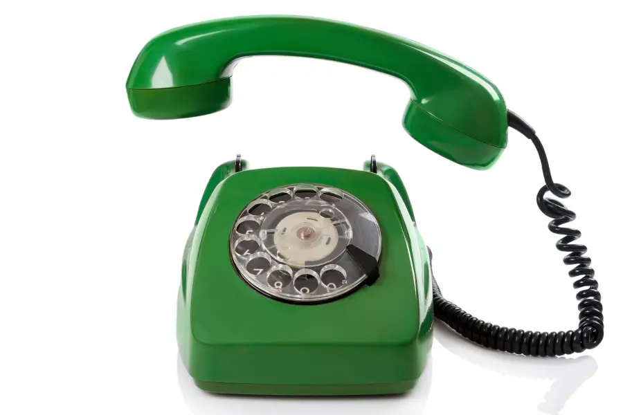 Green vintage rotary telephone with a raised receiver and coiled cord isolated on a white background.