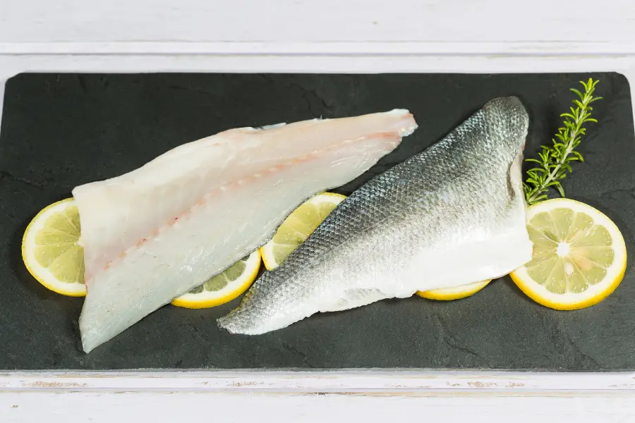Der Sensilab Gutschein hilft auch den gesunde Fischsorten Ratgeber. Fresh raw fish fillets served on a black slate board with lemon slices and a rosemary sprig.