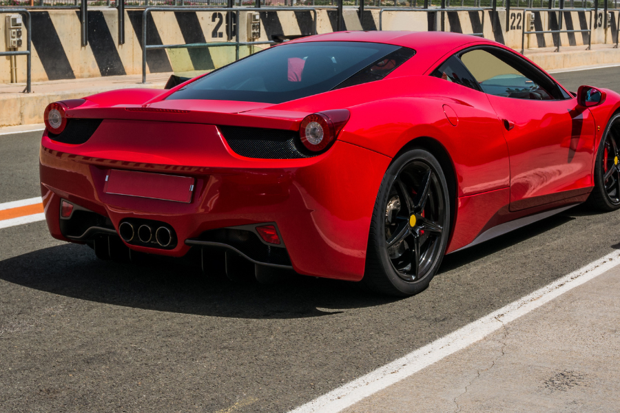 Red luxury sports car driving on a racetrack, viewed from the rear.