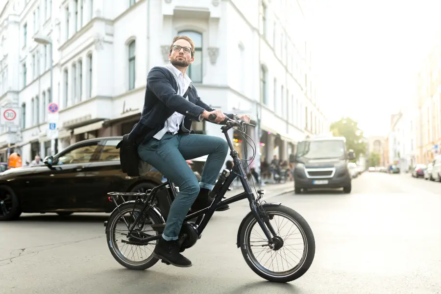 Dela Lebensversicherungen - Wenn einem die Elektromobilität in Deutschland egal ist. Business professional riding an electric bike through a busy city street during his daily commute.