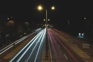 Nighttime city road with long-exposure light trails from moving traffic under streetlights.