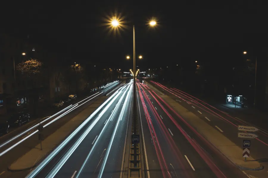 Nighttime city road with long-exposure light trails from moving traffic under streetlights.