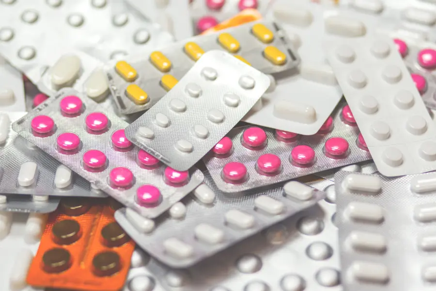 Assorted medicine blister packs with pink, white, yellow, and brown tablets scattered in a close-up view.