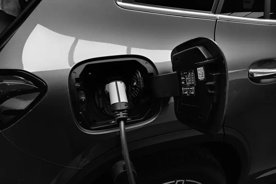 Mit dem Mediamarkt Gutschein auf E-Bikes und co sparen Electric car charging with a plug connected to the charging port in a close-up black-and-white image.