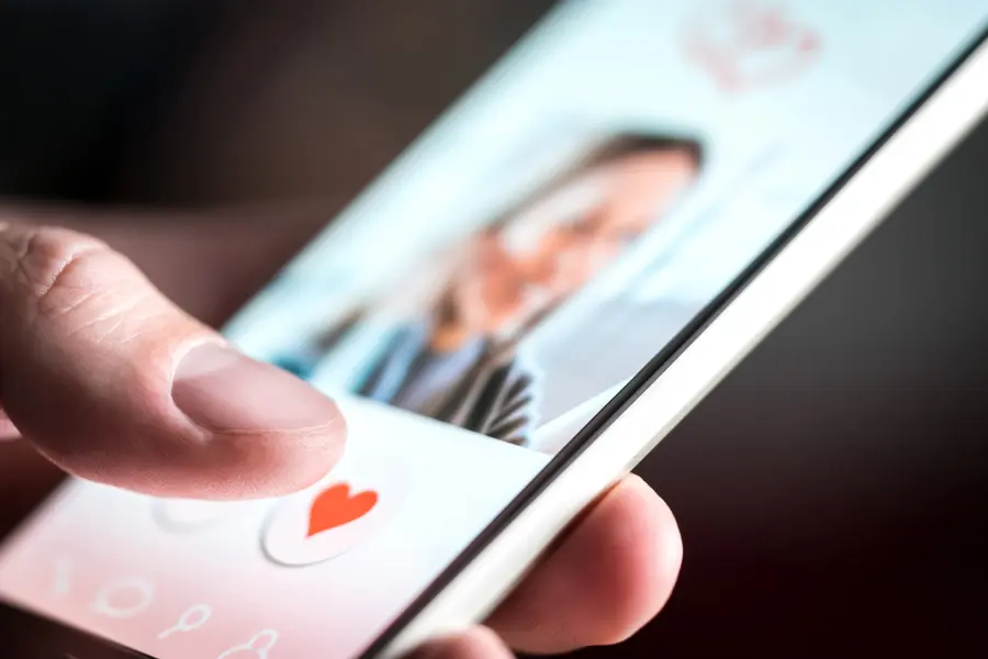 Close-up of a person tapping a heart icon on a smartphone dating app profile.