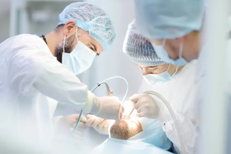 Dental surgeons wearing masks and protective caps performing a procedure on a patient in a clinical operating room.