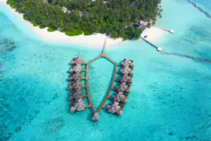 Luftaufnahme eines typischen Luxusresorts auf den Malediven mit Wasservillen in türkisfarbenem Ozean und Palmen am weißen Sandstrand.