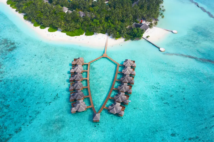 Luftaufnahme eines typischen Luxusresorts auf den Malediven mit Wasservillen in türkisfarbenem Ozean und Palmen am weißen Sandstrand.