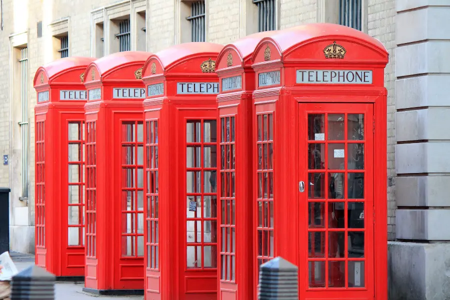Row of iconic red British telephone booths on a city sidewalk in front of a stone building.