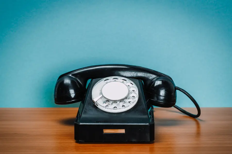 Vintage black rotary telephone on a wooden table against a blue background.