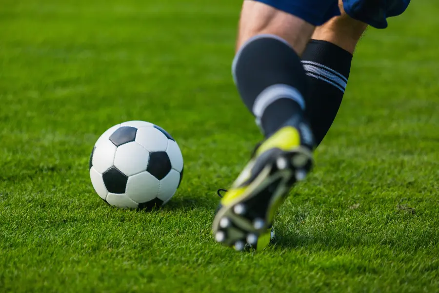 Die Fußballschuhe von Lionel Messi tragen? Das geht ganz einfach mit dem World-of-Football Gutschein. Fußballspieler läuft auf grünem Rasen zum Ball und setzt zum Schuss an.