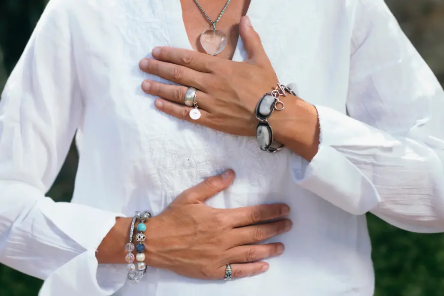 Nahaufnahme einer Person in weißer Kleidung, die beide Hände achtsam auf Brust und Bauch legt – eine typische Haltung zur Durchführung von Atemübungen wie der 4-7-8-Technik.