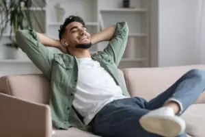 Person liegt entspannt auf einem Sofa und hört Musik über kabellose In-Ear-Kopfhörer im Wohnzimmer