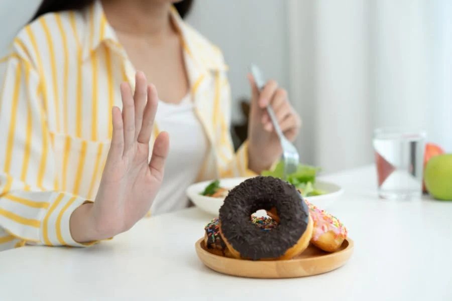 Fasten zwischen Tradition, Religion und moderner Gesundheitsbewegung 2 Person lehnt Donuts auf einem Teller ab und greift stattdessen zu Salat und Wasser