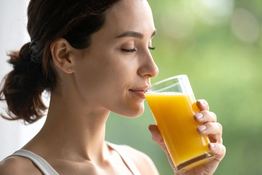 Fasten zwischen Tradition, Religion und moderner Gesundheitsbewegung 3 Frau trinkt ein Glas orangenen Saft vor unscharfem grünem Hintergrund