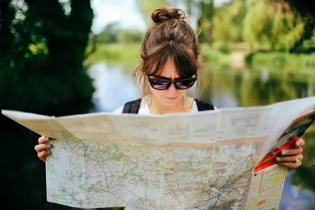 Junge Frau mit Sonnenbrille betrachtet eine große Landkarte vor grünem Naturhintergrund